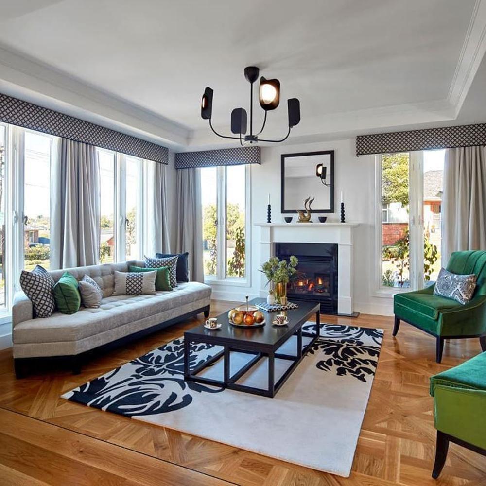 A black Clérachic chandelier with five leaf shades hangs in a bright sitting room with a fireplace, green armchairs and a patterned rug.