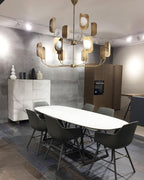 A brass-toned Clérachic chandelier hangs over an oval white table and grey chairs in a kitchen-diner with a stone-clad wall.