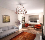 A copper-toned Clérachic chandelier with many arms and lit leaf shades hangs above a sofa in a living room with red armchairs.