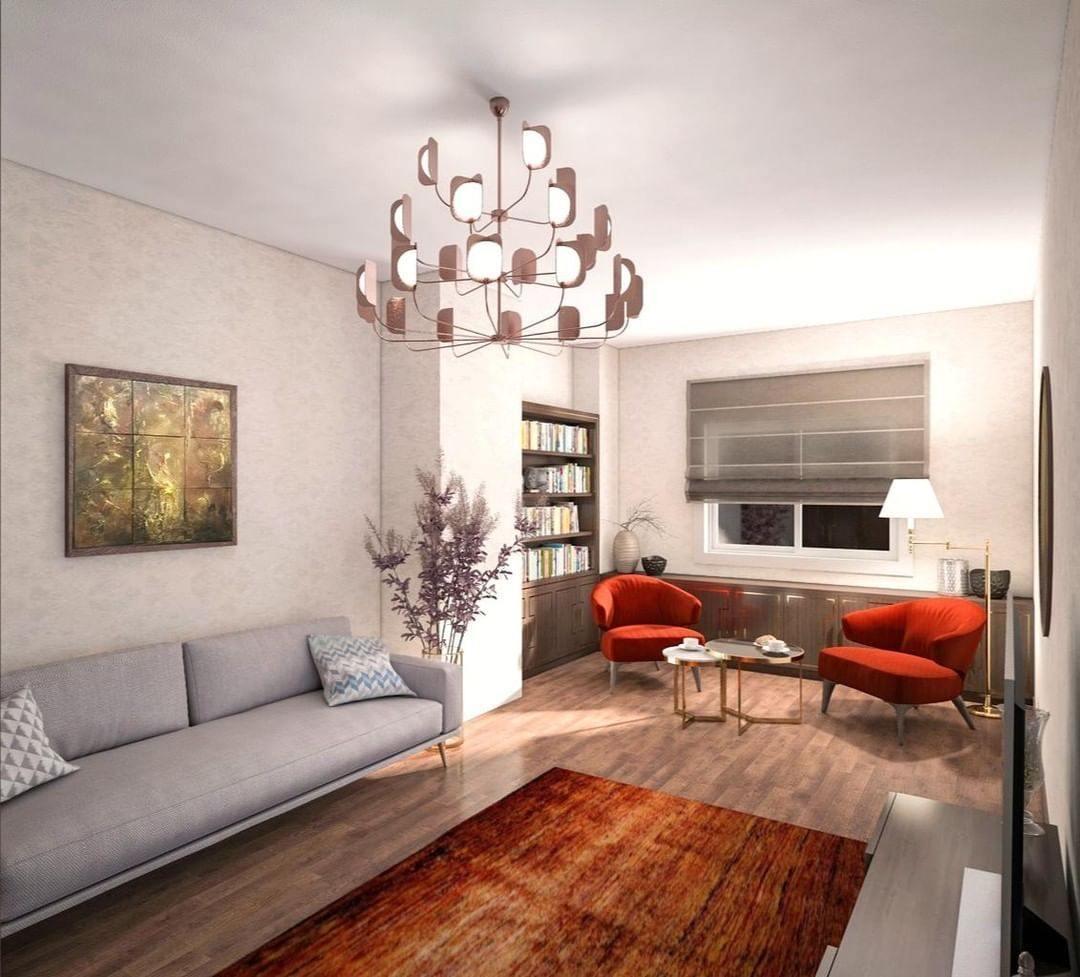 A copper-toned Clérachic chandelier with many arms and lit leaf shades hangs above a sofa in a living room with red armchairs.