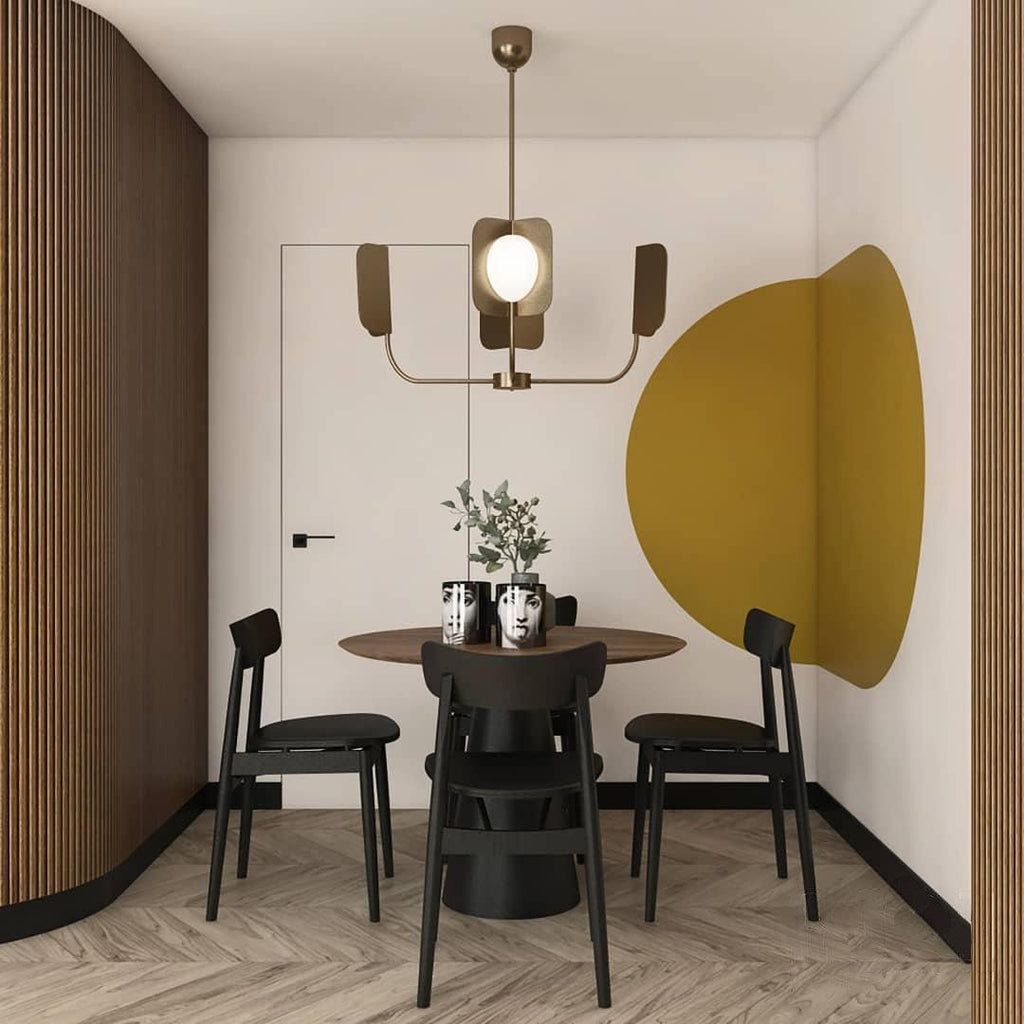 A brass-toned Clérachic chandelier with four leaf shades hangs above a round dining table, in front of a mustard-yellow wall circle.