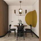 A brass-toned Clérachic chandelier with four leaf shades hangs above a round dining table, in front of a mustard-yellow wall circle.