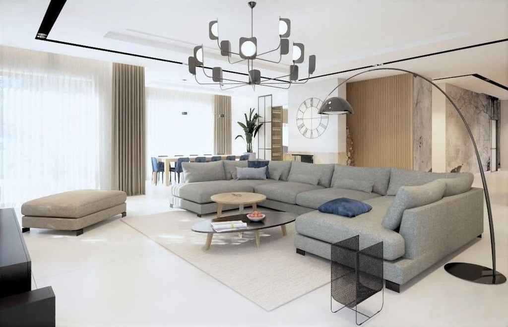 A black Clérachic chandelier with many leaf shades and lit globes hangs above a grey corner sofa and oval coffee tables.