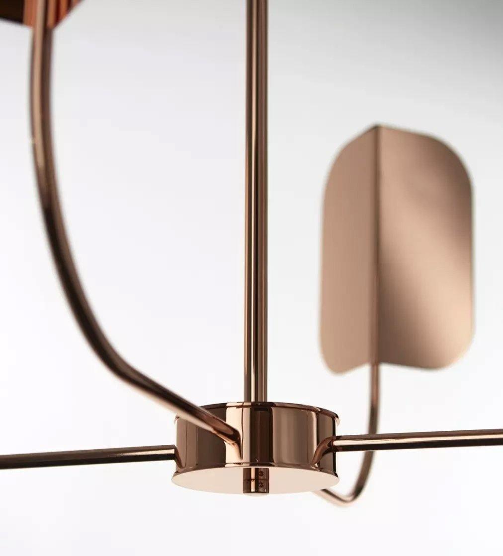 Close view of the copper hub and a curved arm on this Clérachic chandelier, with one soft-focus leaf shade on the right.