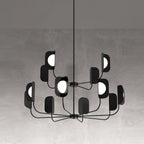 A black Clérachic chandelier in a concrete-look setting, two tiers of arms with leaf shades and glowing white globes.