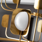 Close view of a lit opal globe in a brass-toned leaf shade on this Clérachic chandelier, with other arms blurred around it.