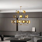 A large brass-toned Clérachic chandelier with three tiers of arms, hung in a grey lounge above a low black table and a sofa.