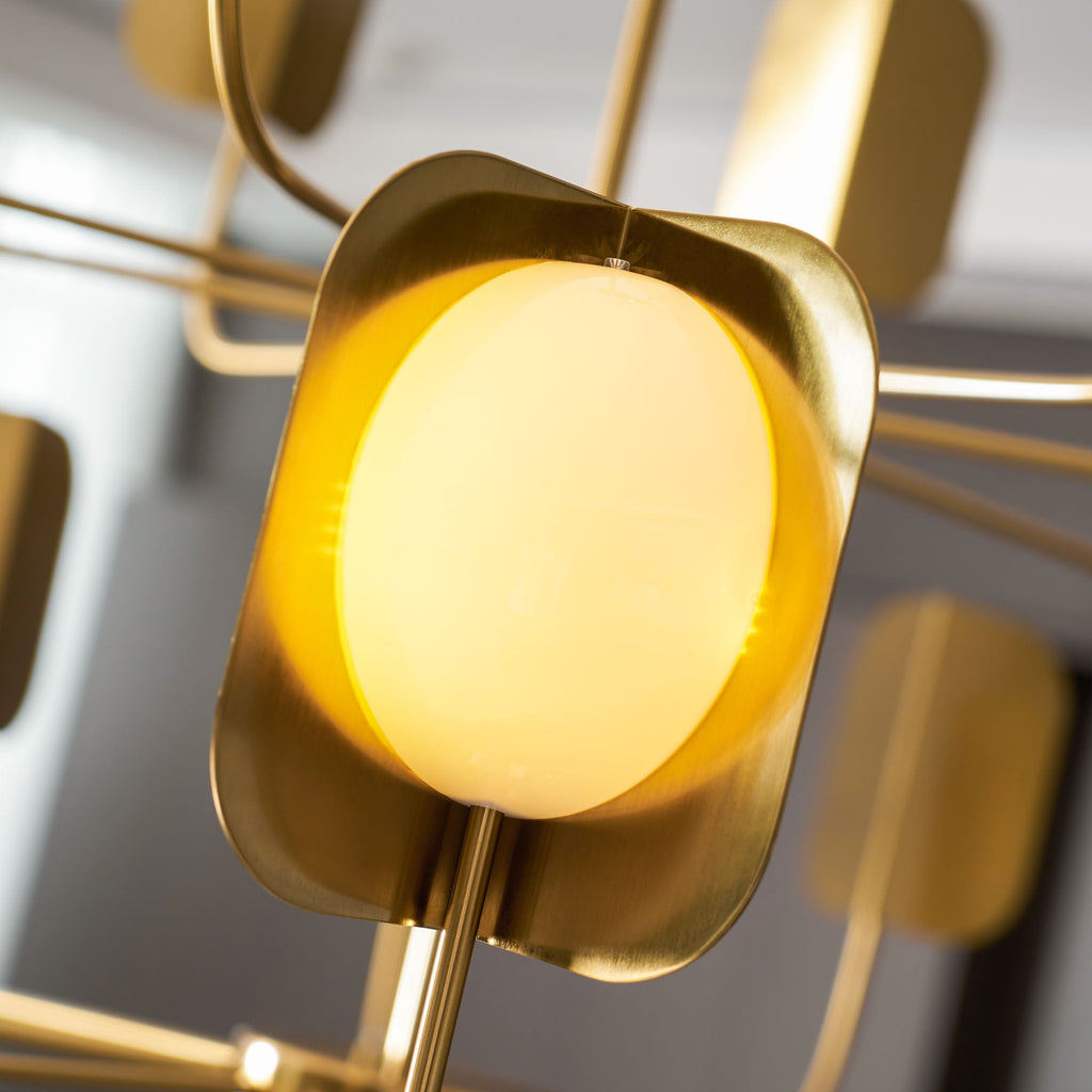 Close view of a glowing yellow-white globe in a brass-toned leaf shade on a Clérachic chandelier, with arms blurred behind.