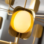 Close view of a glowing yellow-white globe in a brass-toned leaf shade on a Clérachic chandelier, with arms blurred behind.