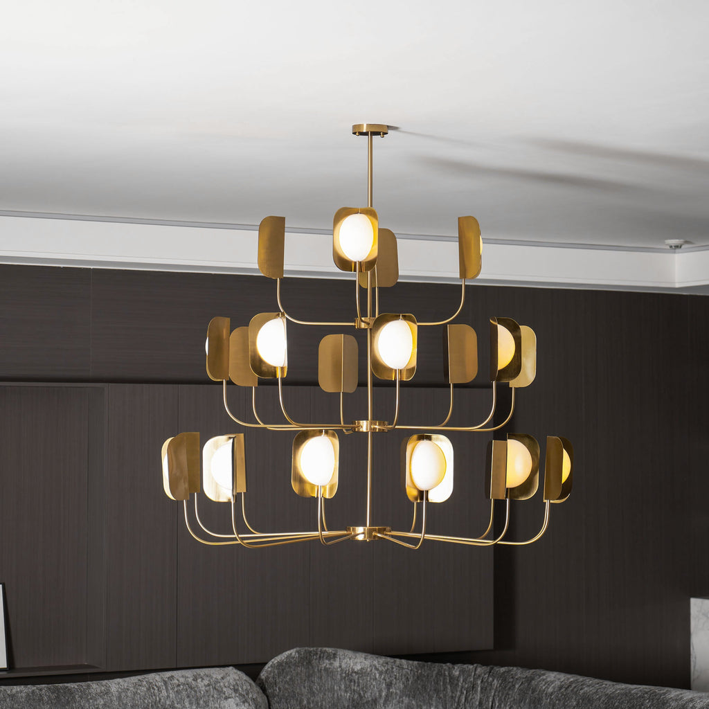 Three tiers of lit leaf shades on a brass-toned Clérachic chandelier, seen straight on above a sofa in a dark panelled room.