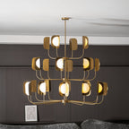 The lit brass-toned Clérachic chandelier seen from the side, its lower tier of arms spread wide above a low table and a small framed print.
