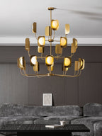 Low view of a brass-toned Clérachic chandelier in a lounge, its three tiers of leaf shades and globes against a dark wall.