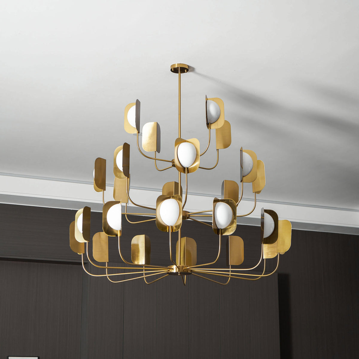 A brass-toned Clérachic chandelier with many leaf shades and unlit white globes, hung from a short rod beneath a white ceiling.