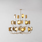 A brass-toned Clérachic chandelier lit warm on a pale backdrop, each globe glowing inside its leaf shade on three tiers.