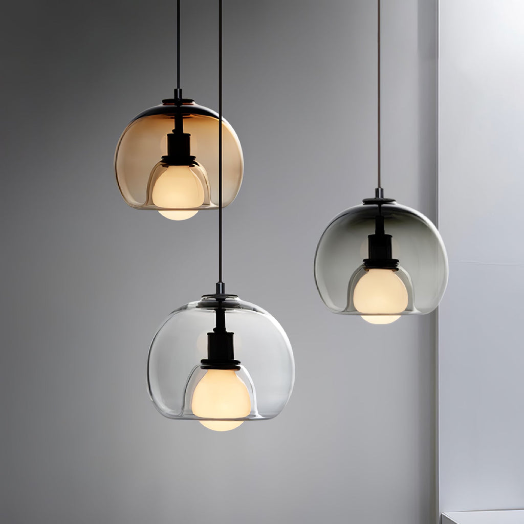 Three Clérachic pendants in cognac, clear and smoke glass hang at different heights against a grey wall, each lit.