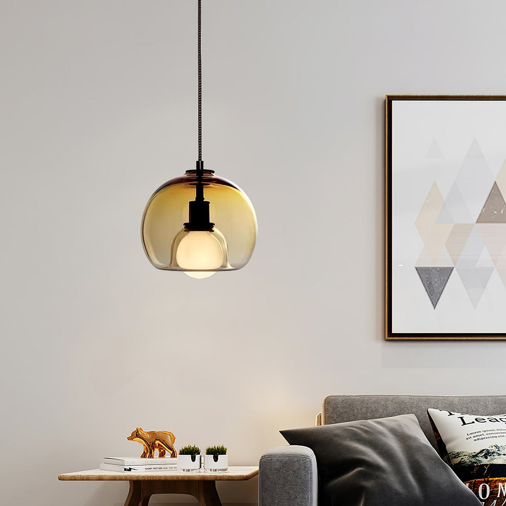 A cognac glass Clérachic pendant glows above a low table and grey sofa, beside a framed geometric print.