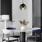 A Clérachic pendant in smoke glass hangs in a white panelled room above a marble table with navy and white chairs.