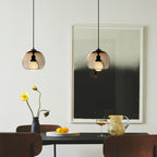Two cognac glass Clérachic pendants hang over a dark dining table beside a large black-and-white framed print.