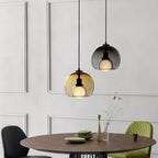 A cognac and a smoke Clérachic pendant hang over a round walnut table with a green chair in a panelled dining room.