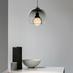 A smoke glass Clérachic pendant hangs in a pale room above a stone bowl and a dark vase on a table edge.