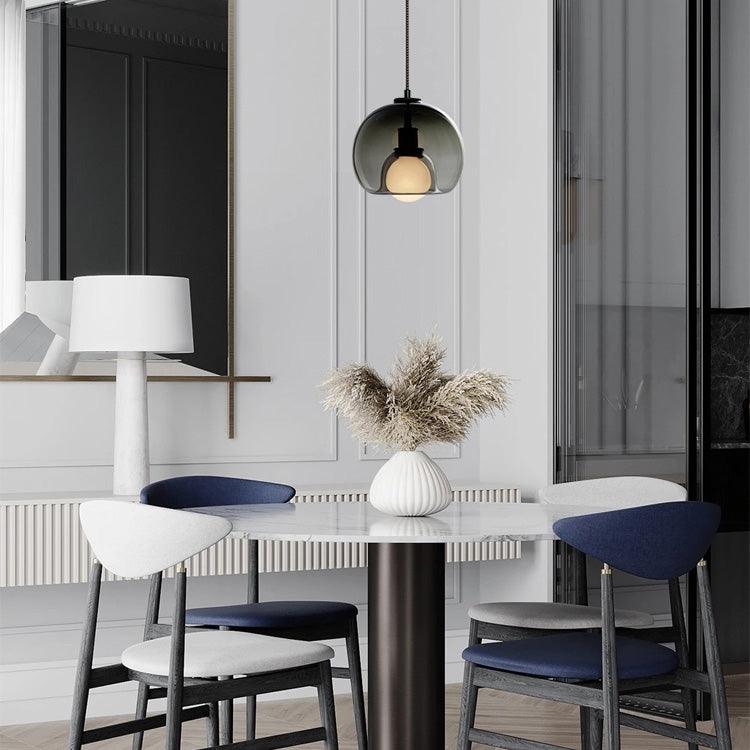 A smoke glass Clérachic pendant hangs in a white panelled room above a table with a vase and navy chairs.