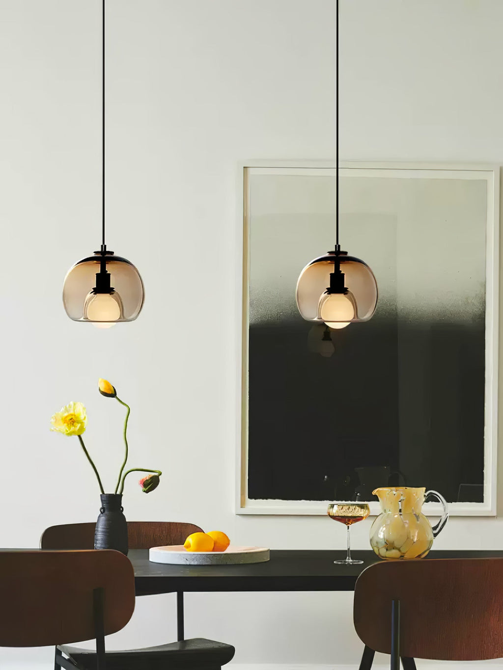 Two cognac glass Clérachic pendants hang above a dark table with yellow flowers and a large framed monochrome print.