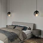 A smoke glass Clérachic pendant on each side of a bed, hung from black cords against a pale wall.
