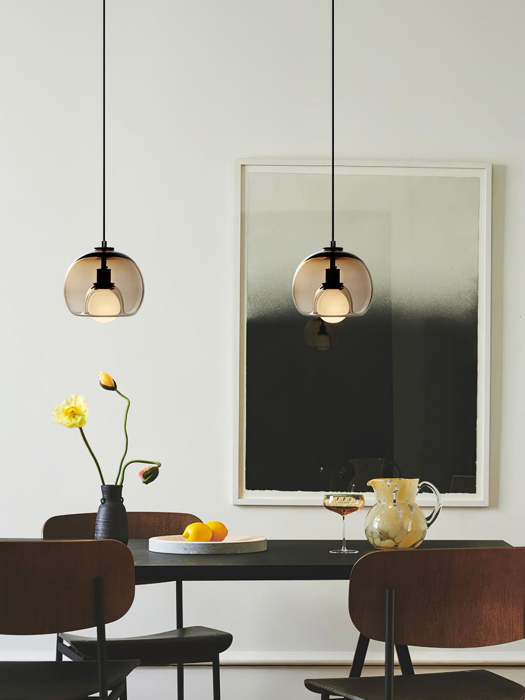 Two cognac Clérachic pendants hang over a dark table with a flower vase and a black-and-white print behind.