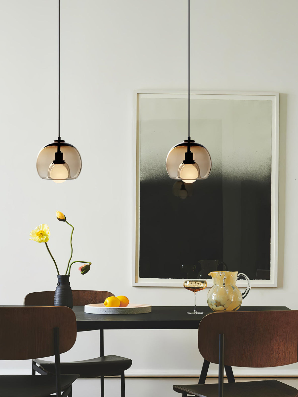 Two cognac Clérachic pendants hang over a dark table with a flower vase and a black-and-white print behind.
