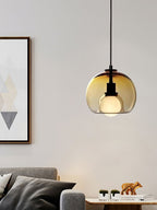 A cognac glass Clérachic pendant hangs by a framed geometric print, with a grey sofa and cushions below.