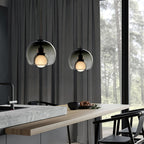 Two smoke glass Clérachic pendants hang beside tall grey curtains over a stone counter in a forest-view room.