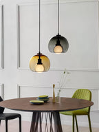 A cognac and a smoke Clérachic pendant hang above a round walnut table in a white panelled room with a green chair.