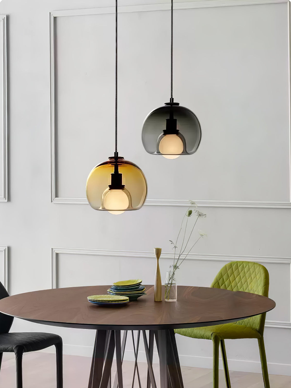 A cognac and a smoke Clérachic pendant hang above a round walnut table in a white panelled room with a green chair.