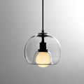 A clear glass Clérachic pendant on a black cord, shown on a grey gradient backdrop with its frosted bulb lit.