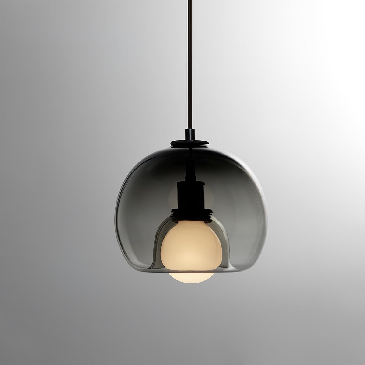 A smoke glass Clérachic pendant on a black cord, with its bulb lit and a soft grey gradient behind.