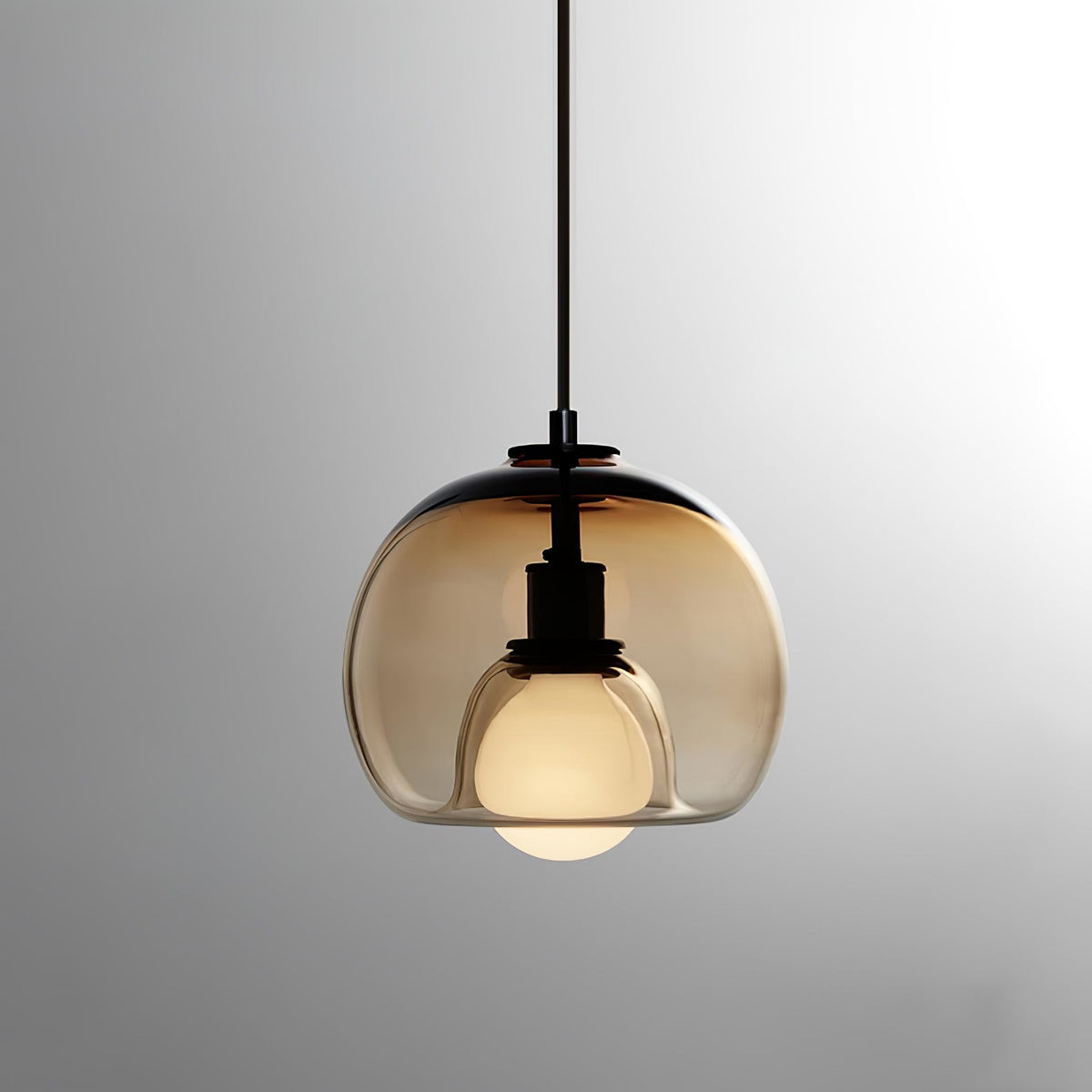 A cognac glass Clérachic pendant on a black cord, its frosted bulb lit against a soft grey gradient.