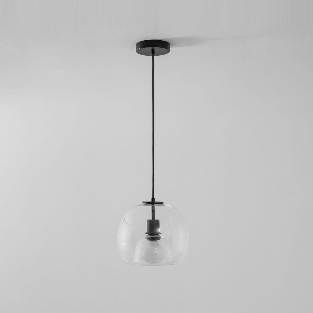 A clear glass Clérachic pendant hangs from a round black ceiling canopy on a black cord, against a pale grey wall.
