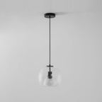 A clear glass Clérachic pendant hangs from a round black ceiling canopy on a black cord, against a pale grey wall.