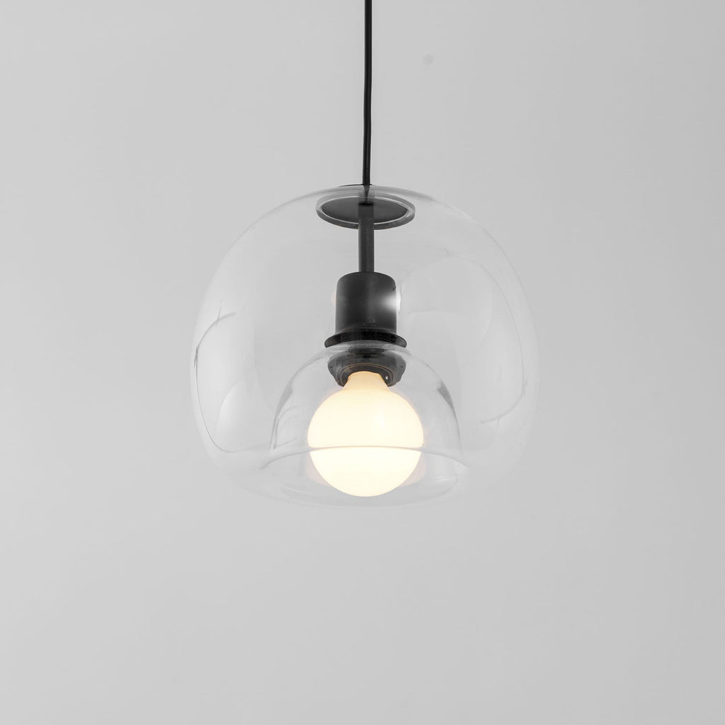 Close view of the clear double-layer glass of this Clérachic pendant, with a frosted bulb and black socket inside.