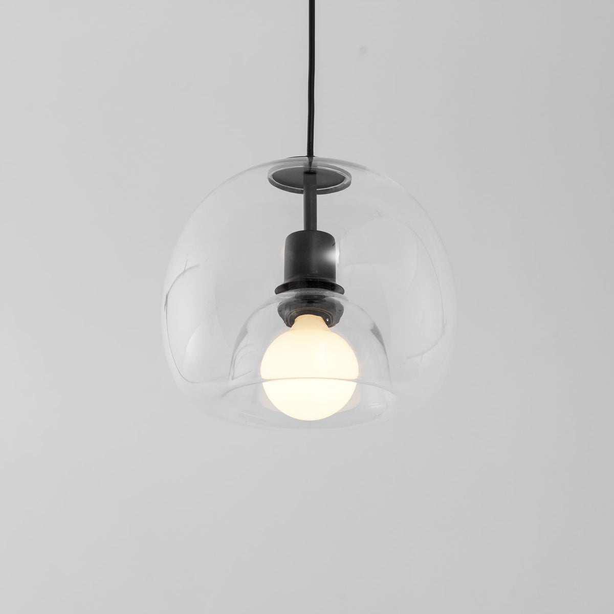 Close view of the clear double-layer glass of this Clérachic pendant, with a frosted bulb and black socket inside.