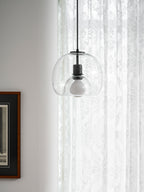 A clear glass Clérachic pendant glows softly against lace curtains, beside a dark framed print.