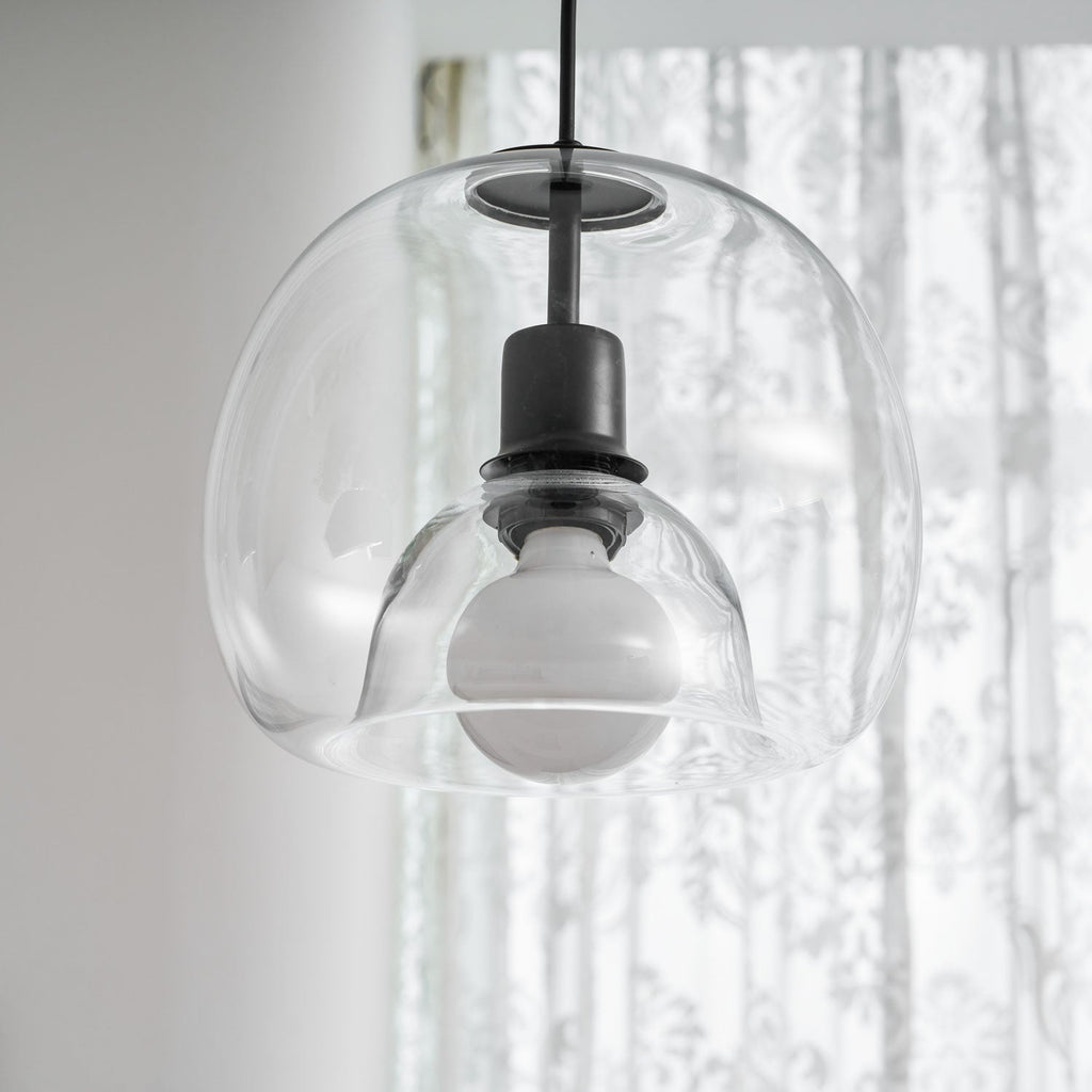 Close view of the inner glass dome and frosted bulb in this Clérachic pendant, in front of sheer curtains.