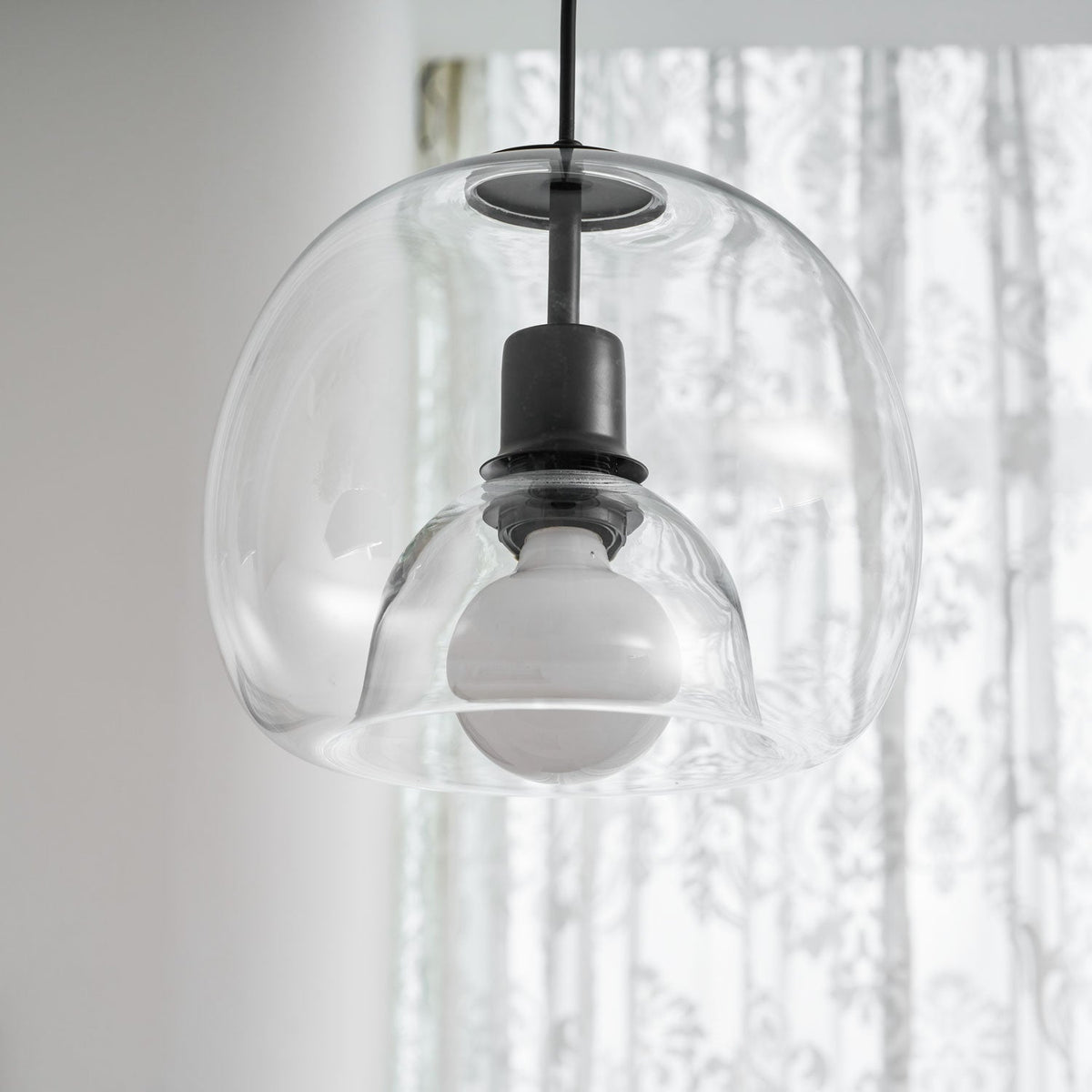 Close view of the inner glass dome and frosted bulb in this Clérachic pendant, in front of sheer curtains.