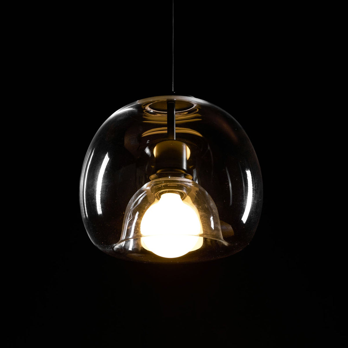 Close view of the double-layer clear glass on this Clérachic pendant, glowing warm against a black backdrop.