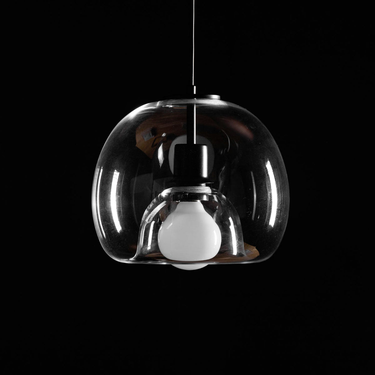 Close view of the clear glass shade, frosted bulb and black socket on this unlit Clérachic pendant in a dark room.