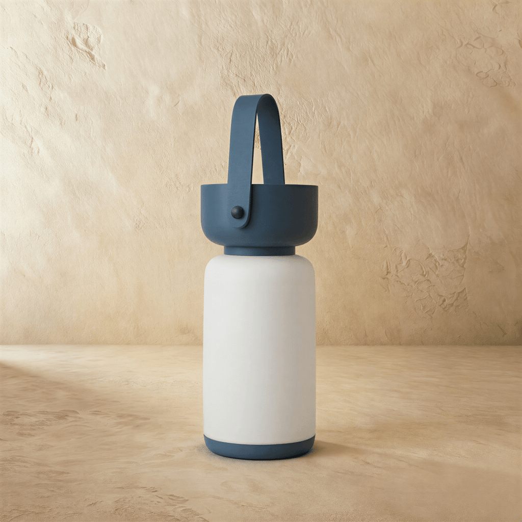 Clérachic cordless cylinder lamp switched off, a white frosted body with a blue handle and base against plaster.