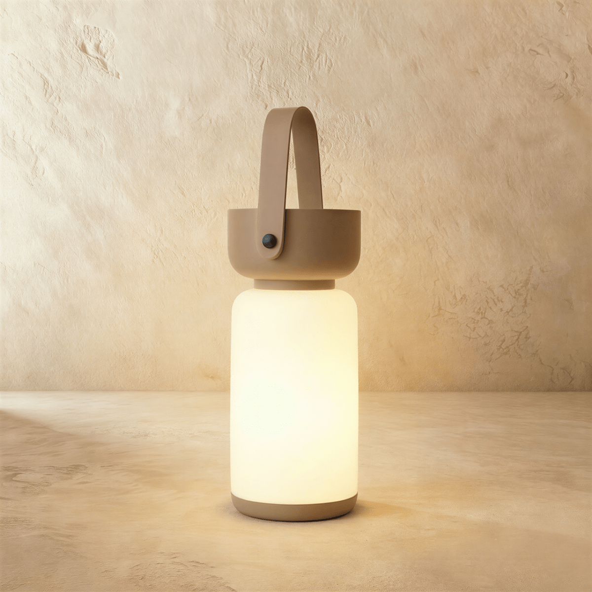 Clérachic cordless cylinder lamp lit warm white, with a taupe-brown handle and base on a limewashed plaster backdrop.
