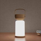 Clérachic cordless cylinder lamp glowing bright white with a brown handle, on a wooden shelf beside a stack of books.