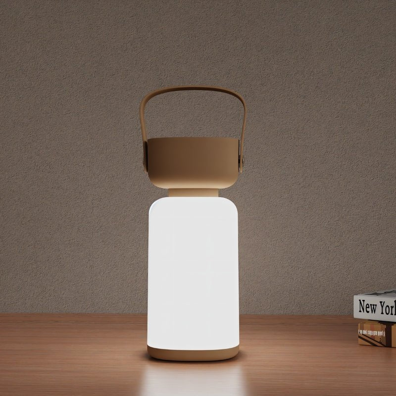 Clérachic cordless cylinder lamp glowing bright white with a brown handle, on a wooden shelf beside a stack of books.