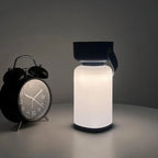 Clérachic cordless cylinder lamp with a dark handle giving a soft glow on a grey table next to a black alarm clock.